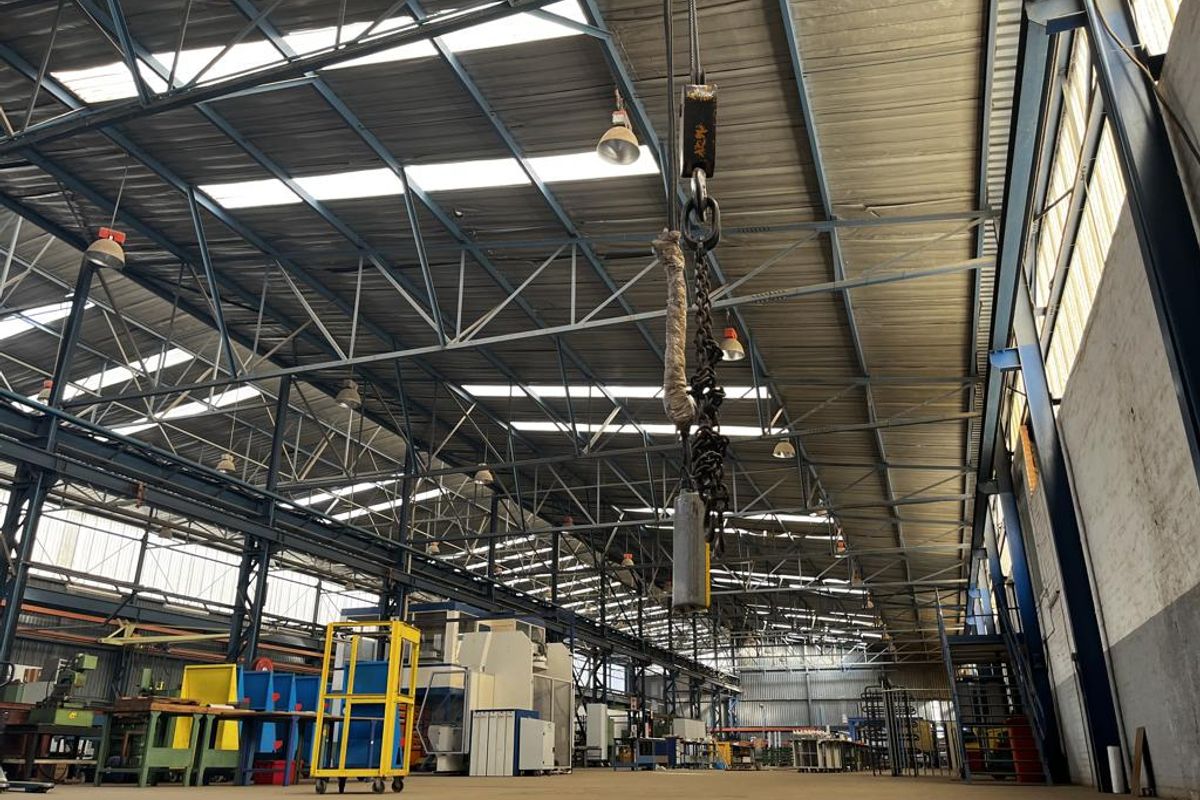 Spacious industrial warehouse featuring a high steel truss roof, overhead crane system, natural skylight illumination, and durable concrete flooring.