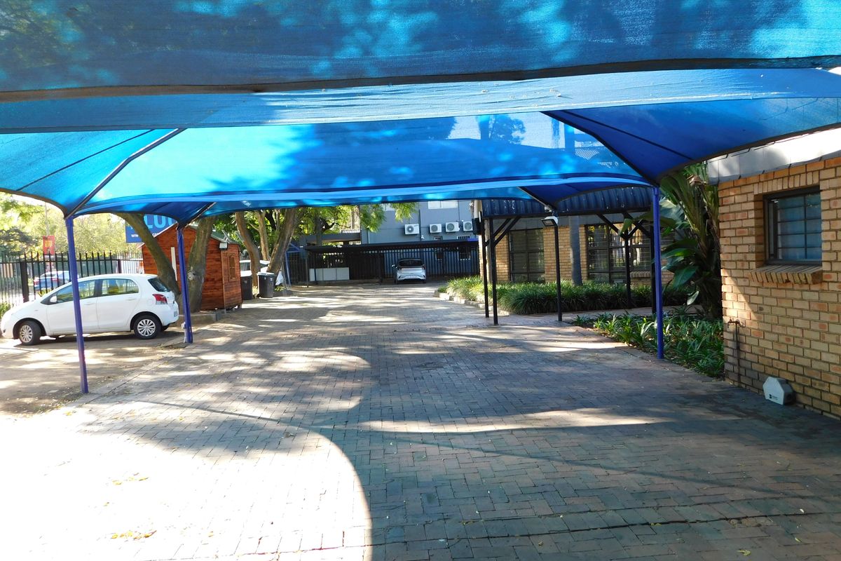 A paved driveway area featuring a blue shade cloth carport structure, providing covered parking space for the office property.