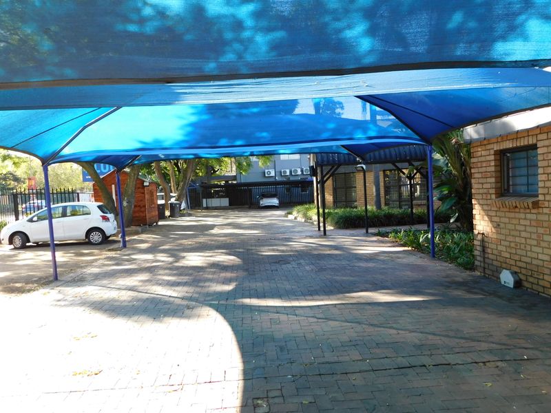 A paved driveway area featuring a blue shade cloth carport structure, providing covered parking space for the office property.