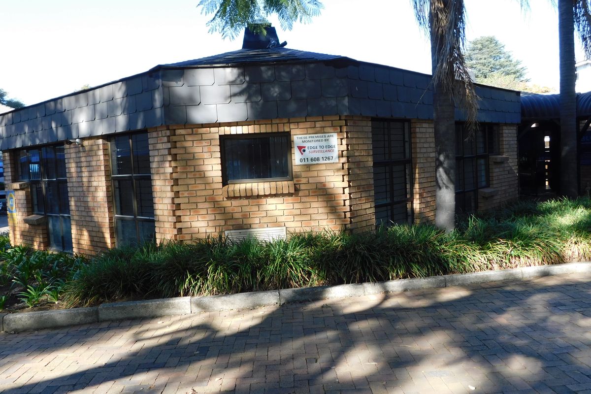 Exterior view of a face brick office building featuring a tiled roof, security window bars, and a paved driveway entrance.