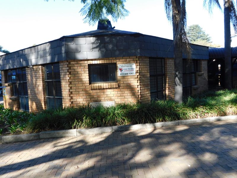 Exterior view of a face brick office building featuring a tiled roof, security window bars, and a paved driveway entrance.