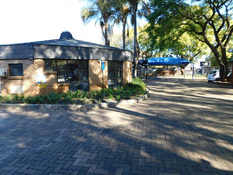 Front exterior view of the office property featuring a brick facade, paved driveway, and shaded parking area with established trees.