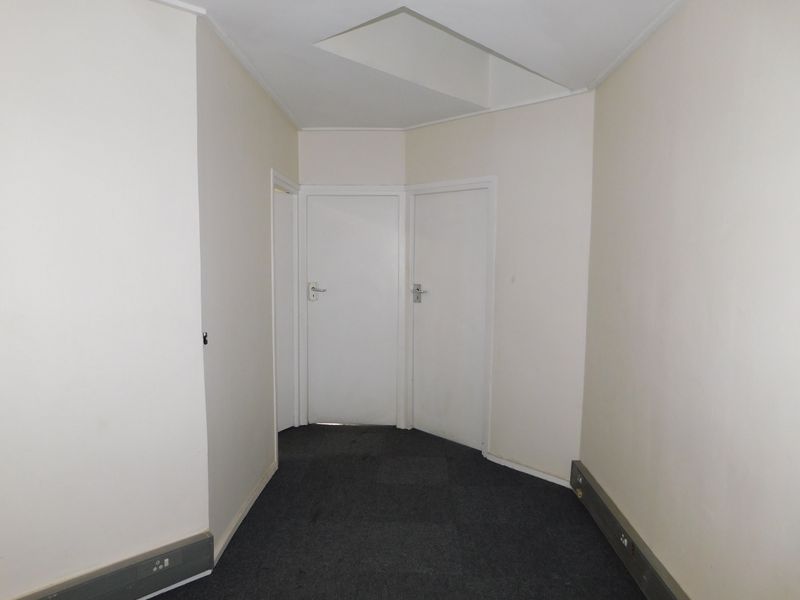 A functional office hallway featuring neutral walls, grey carpeting, and integrated electrical trunking along the baseboards.