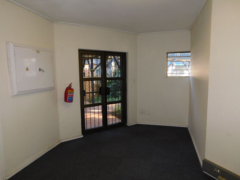 An empty office space featuring carpeted flooring, a security gate, and a wall-mounted fire extinguisher.