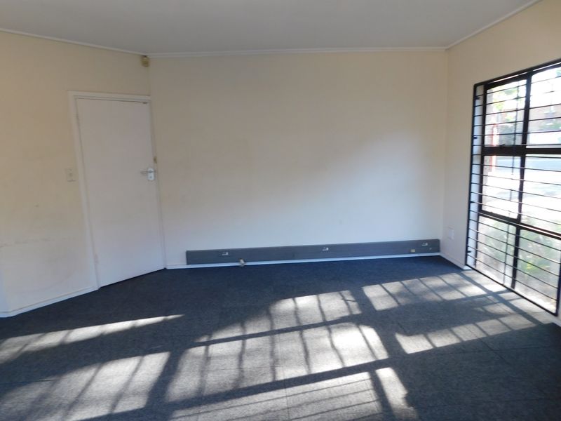 An empty office space featuring grey carpeting, security bars on the windows, and wall-mounted electrical trunking.