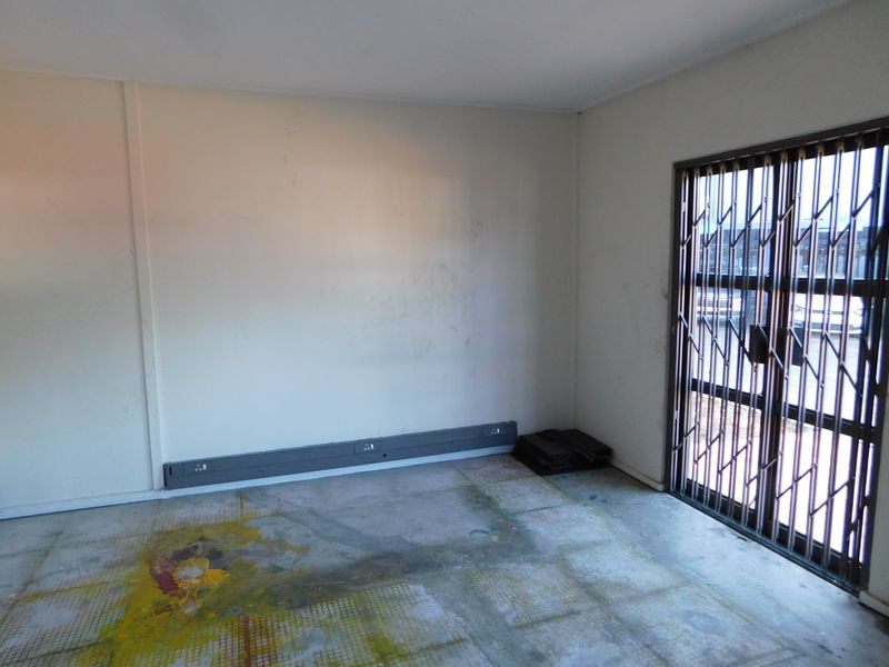 An empty office space featuring a concrete floor, wall-mounted electrical trunking, and a secure metal gate at the entrance.