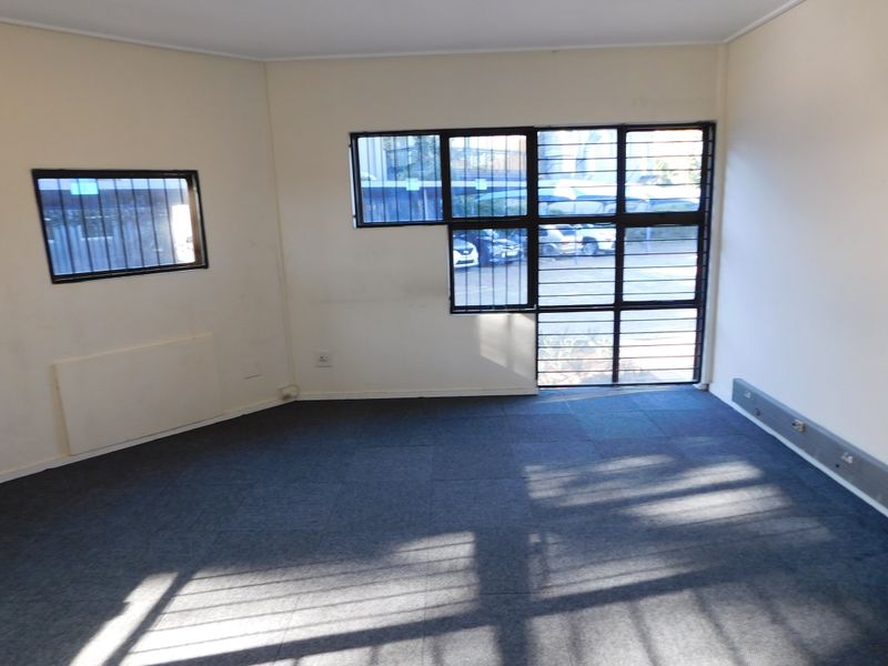 An empty office space featuring carpet tiles, security bars on windows, and integrated electrical trunking along the baseboards.