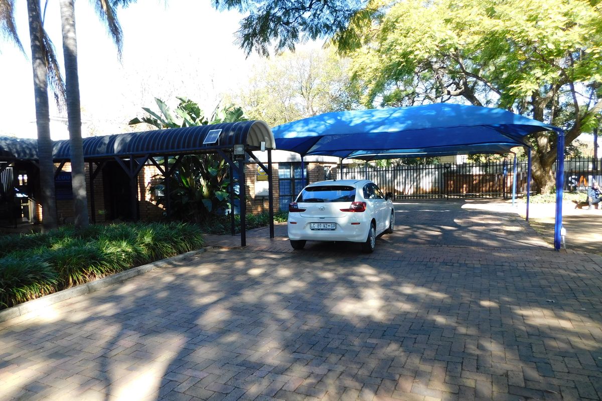 Front exterior view of the office property featuring a paved driveway, shaded parking structure, and covered walkway entrance.