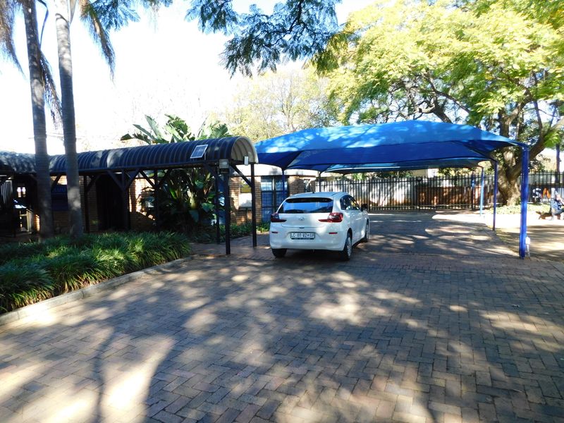 Front exterior view of the office property featuring a paved driveway, shaded parking structure, and covered walkway entrance.