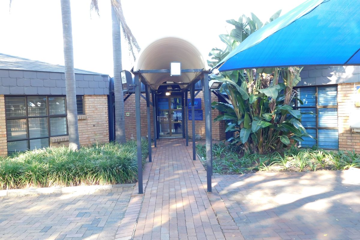 Front entrance of the office building featuring a paved walkway, covered entryway, and established garden landscaping.