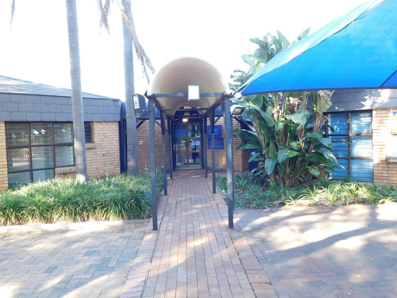 Front entrance of the office building featuring a paved walkway, covered entryway, and established garden landscaping.