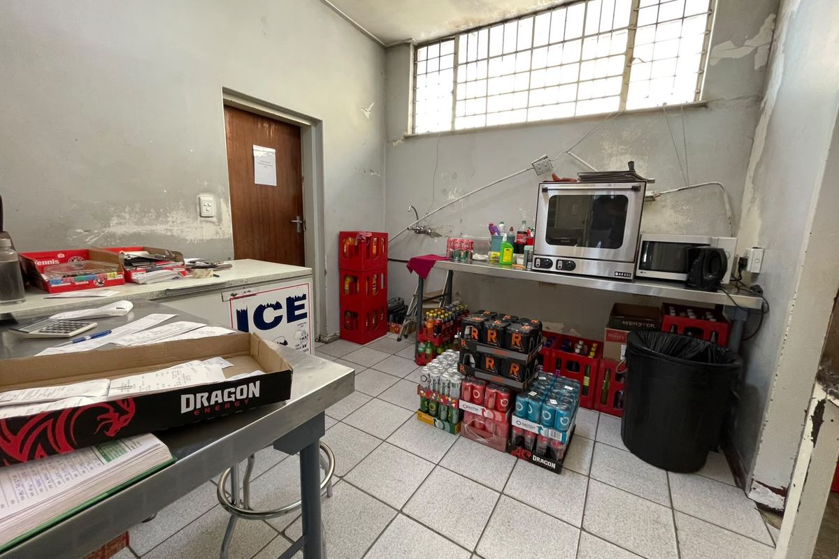 A functional utility or scullery area featuring tiled flooring, stainless steel prep surfaces, and a security-grille window, currently showing signs of wear.