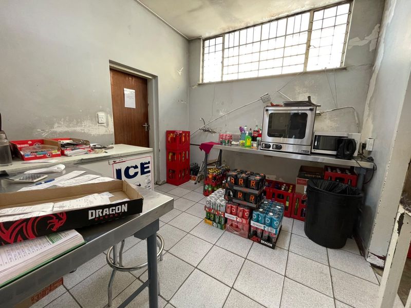 A functional utility or scullery area featuring tiled flooring, stainless steel prep surfaces, and a security-grille window, currently showing signs of wear.