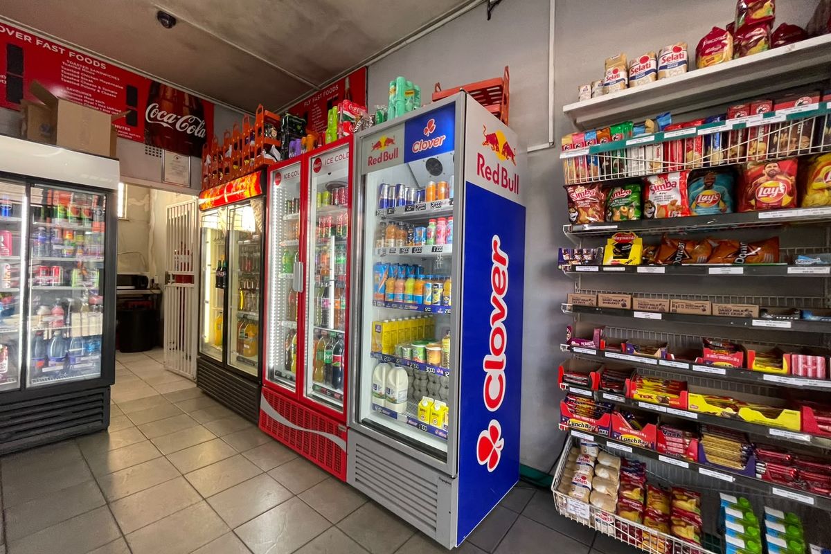 A commercial retail space featuring tiled flooring, multiple commercial refrigeration units, and metal shelving for product display.
