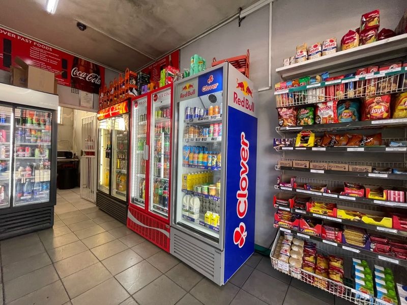 A commercial retail space featuring tiled flooring, multiple commercial refrigeration units, and metal shelving for product display.