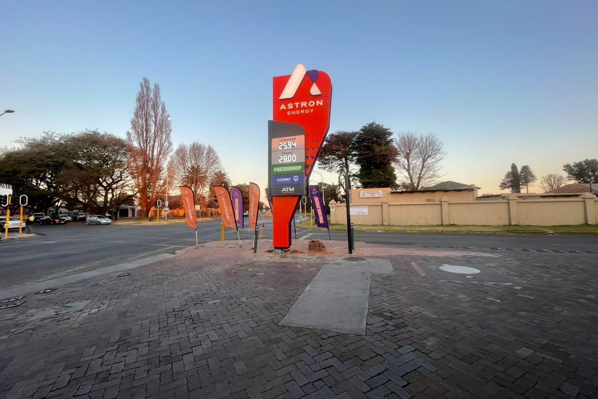 A street-level view of a commercial fuel station entrance featuring a prominent Astron Energy price totem sign and paved forecourt area.