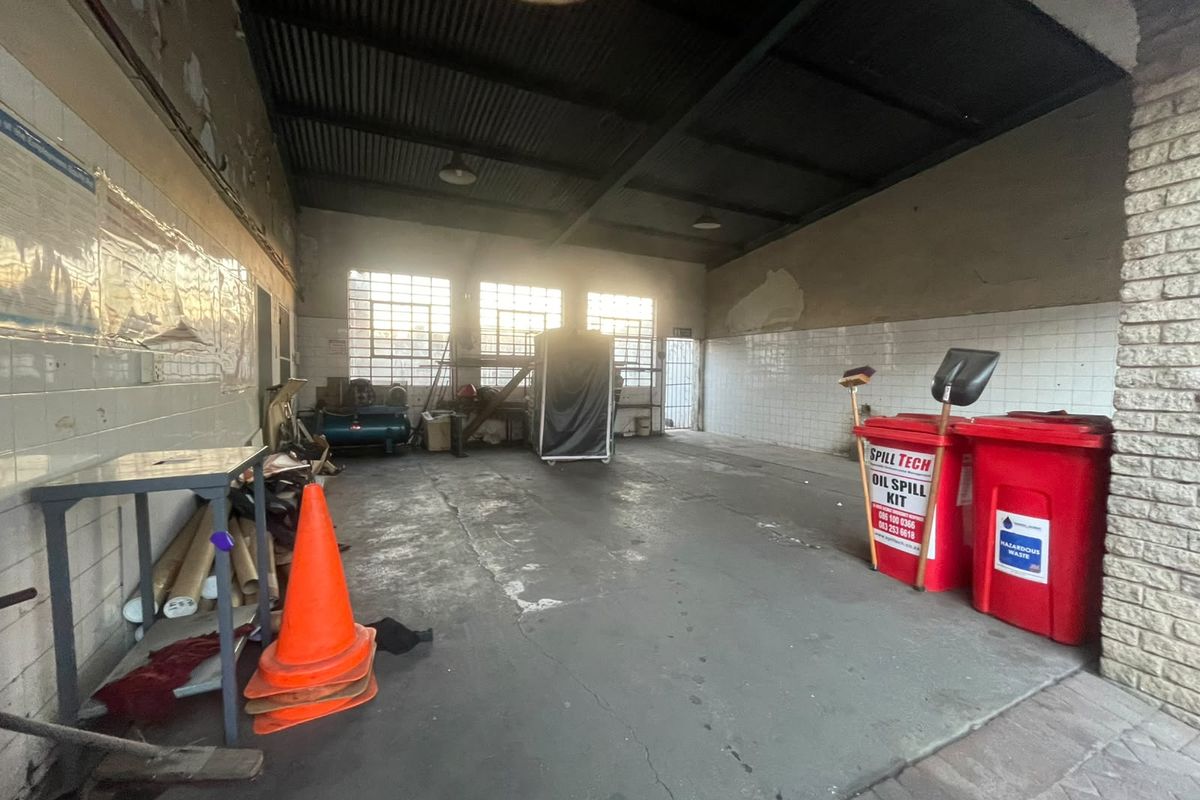 A functional utility or workshop space featuring concrete flooring, tiled wall sections, and high corrugated metal ceilings with exposed trusses.