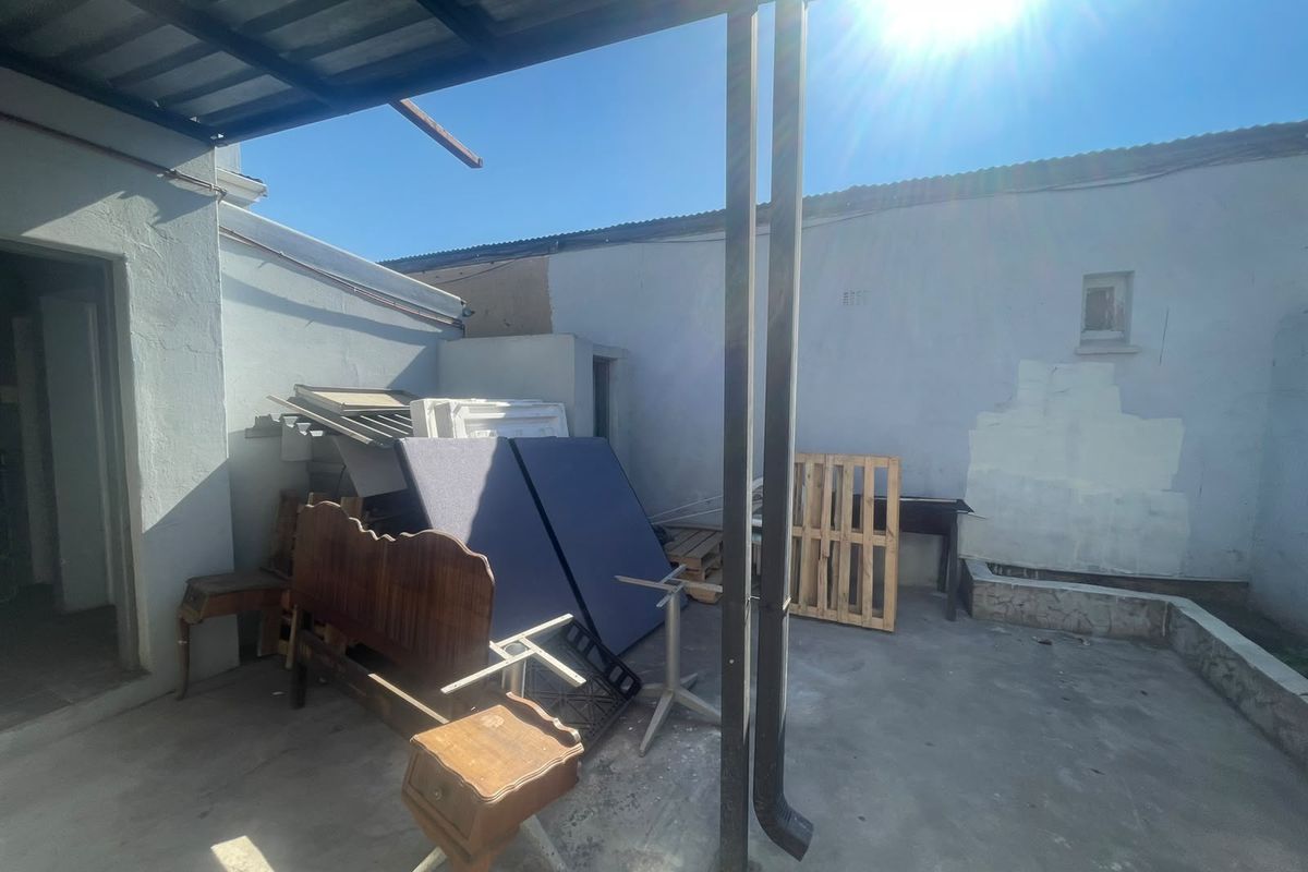 An outdoor covered patio area featuring concrete flooring and metal support columns, currently requiring maintenance and cosmetic updates to the surrounding walls.