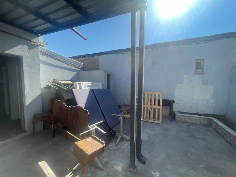 An outdoor covered patio area featuring concrete flooring and metal support columns, currently requiring maintenance and cosmetic updates to the surrounding walls.