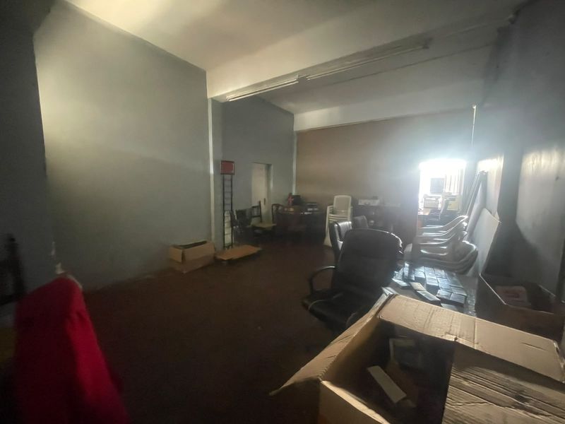 An open-plan retail or office space featuring high ceilings, fluorescent lighting, and neutral wall finishes, currently used for storage.