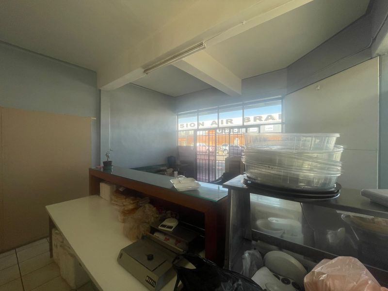 Open plan retail space featuring a service counter, large display window with security gate, and tiled flooring, suitable for various commercial business operations.