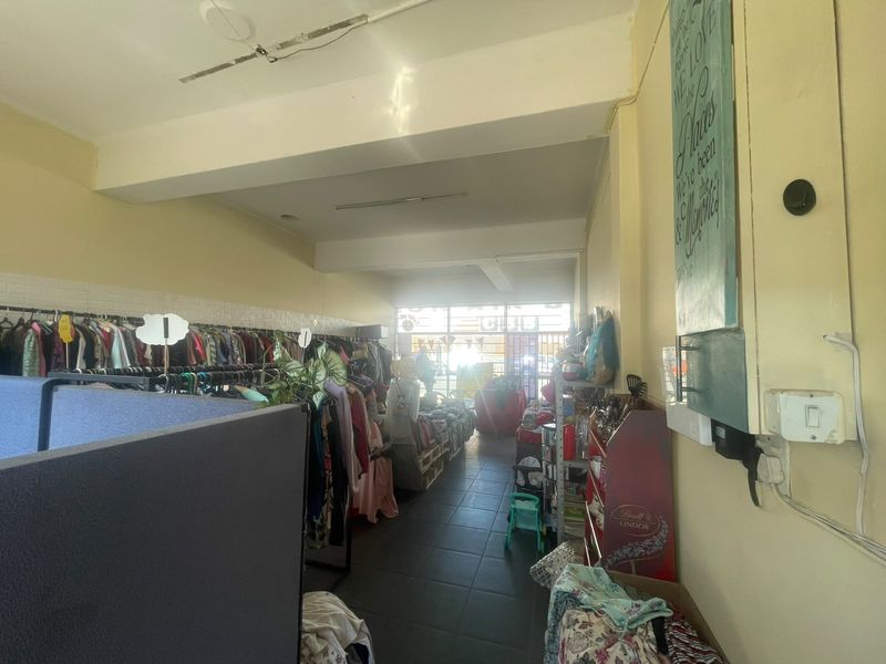 Open-plan retail space featuring tiled flooring, exposed ceiling beams, and a glass storefront, currently utilized for clothing display.