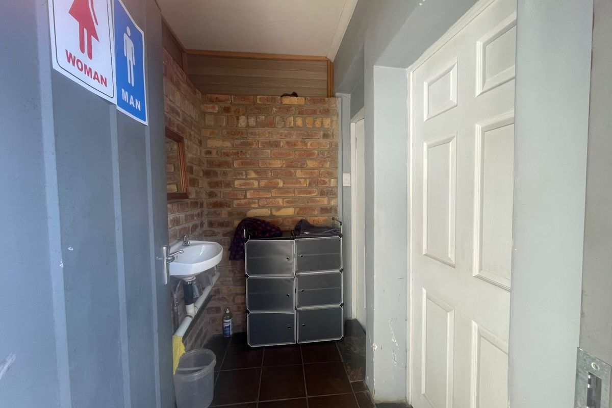 A functional restroom area featuring exposed brickwork, a wall-mounted basin, and tiled flooring, providing basic utility for a retail environment.