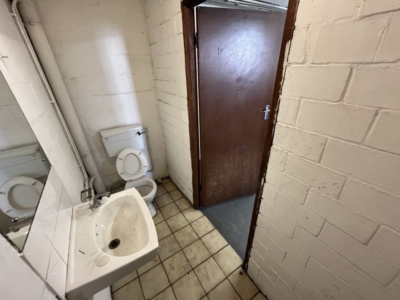 A basic industrial-style bathroom featuring a wall-mounted basin, ceramic toilet, and painted brick walls with tiled flooring.