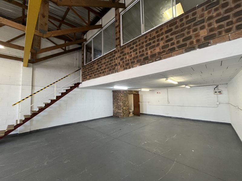 Spacious industrial utility area featuring a mezzanine level, exposed brickwork, timber roof trusses, and a dedicated internal toilet facility.