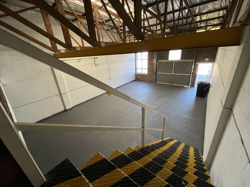 An open-plan industrial utility space featuring exposed timber roof trusses, painted brick walls, and a steel staircase with high-visibility safety treads.