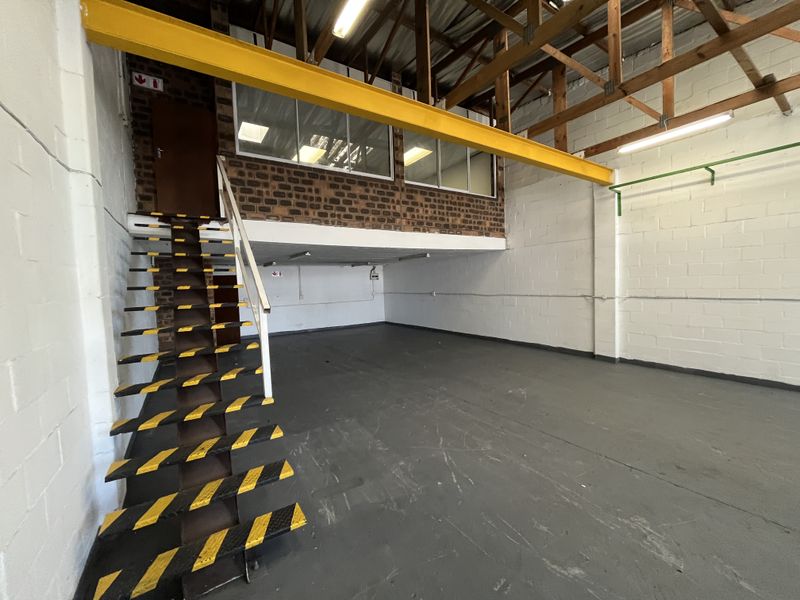 Industrial warehouse space featuring a mezzanine level, steel staircase, exposed timber roof trusses, and durable painted concrete flooring.