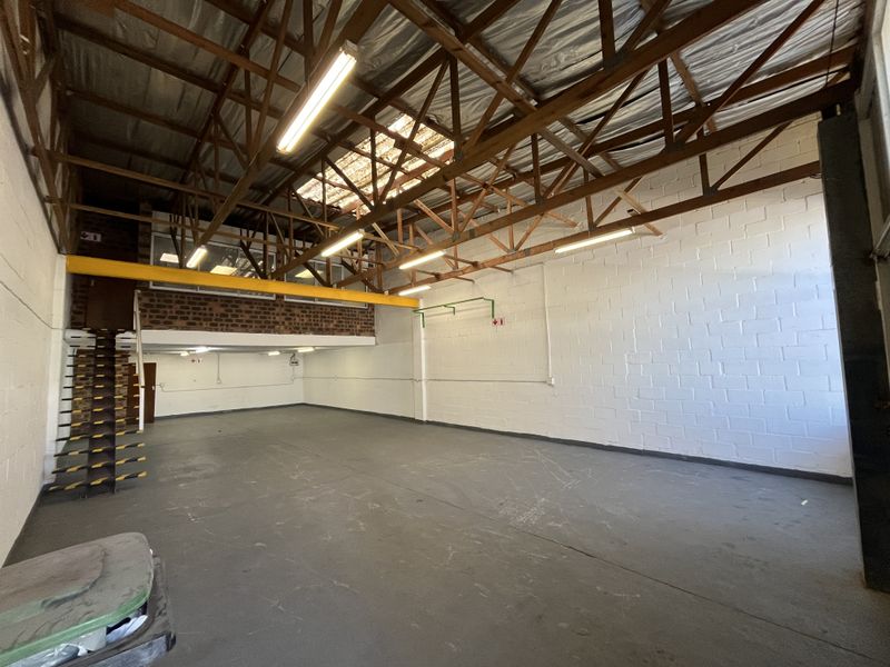 Spacious industrial warehouse unit featuring high ceilings with exposed timber trusses, a mezzanine level, steel staircase, and durable concrete flooring.