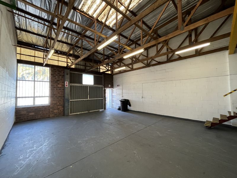 Spacious industrial utility area featuring exposed timber roof trusses, translucent skylights, painted concrete flooring, and secure metal access doors.