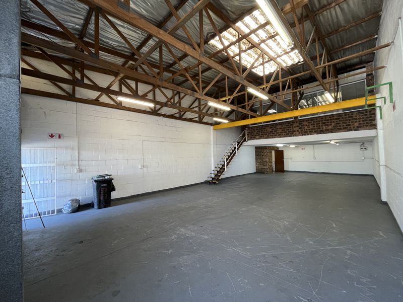 Spacious industrial warehouse unit featuring high ceilings with exposed timber trusses, a mezzanine level, steel staircase, and durable concrete flooring.