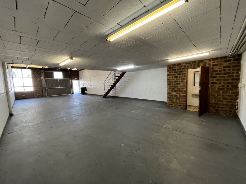 Spacious industrial utility area featuring concrete flooring, exposed brick walls, fluorescent lighting, and an integrated bathroom, suitable for various commercial or storage purposes.