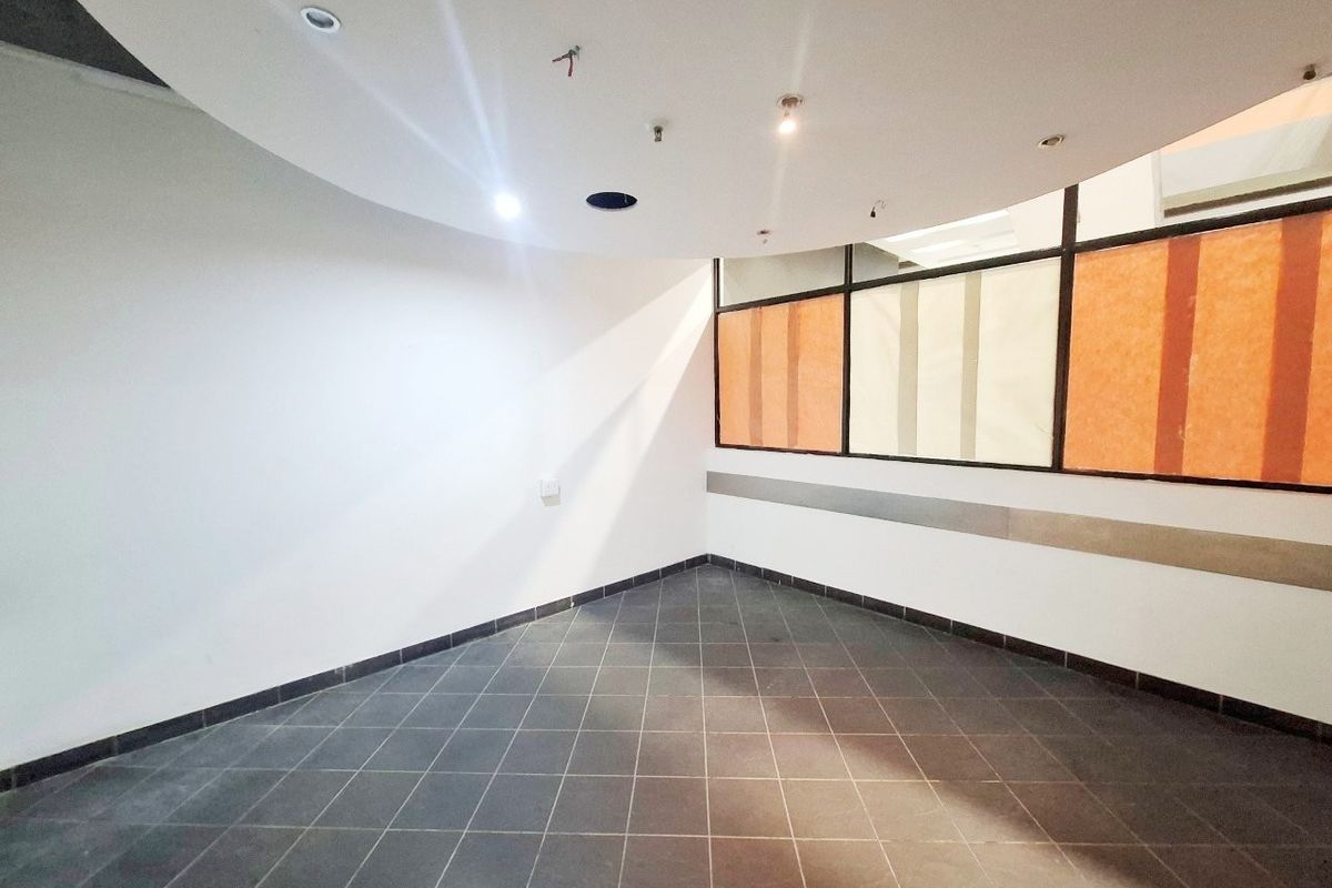 An empty commercial retail space featuring dark tiled flooring, a partitioned glass wall, and recessed ceiling lighting with some fixtures currently missing.