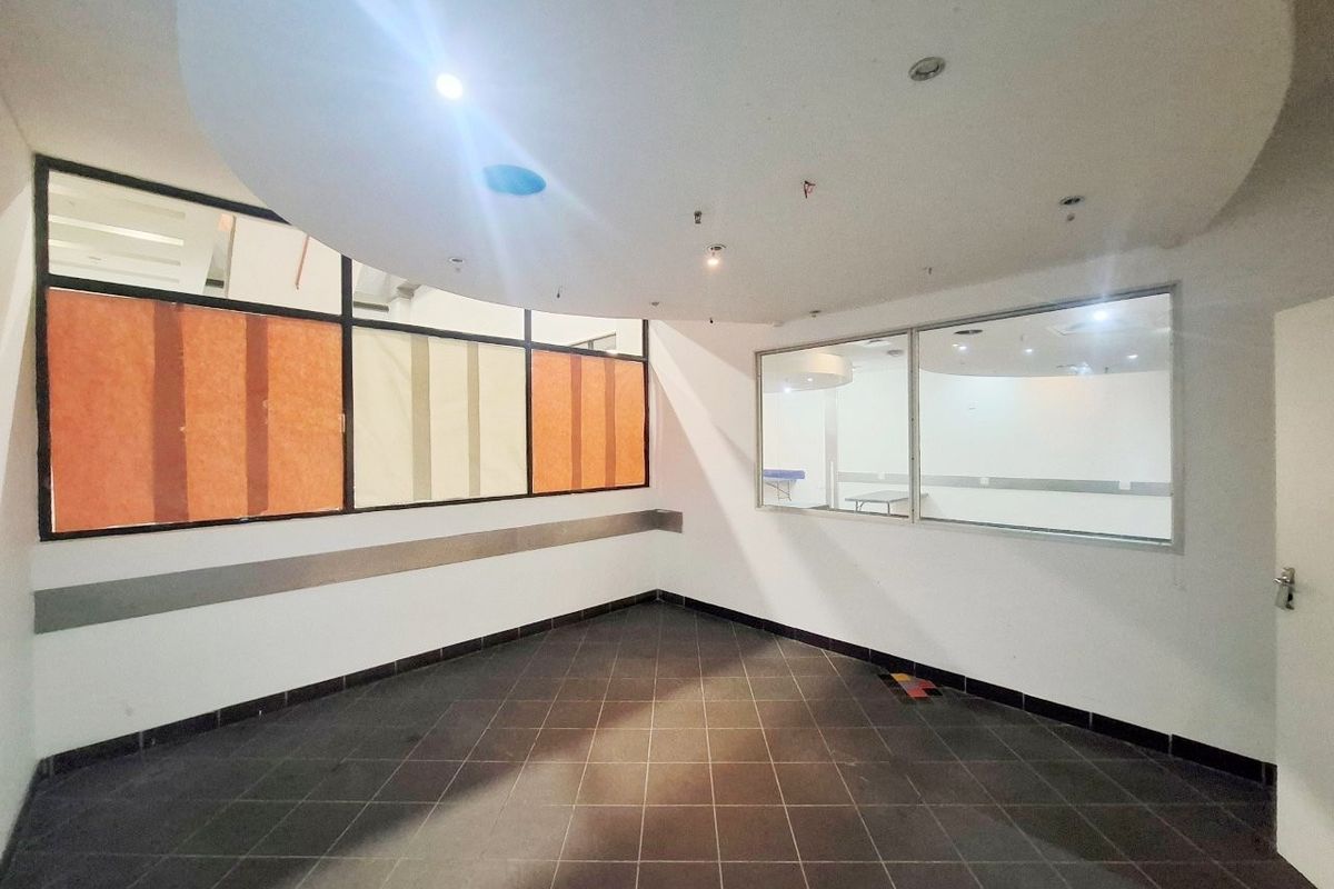 An empty open-plan retail space featuring tiled flooring, a recessed ceiling design, and large glass partitions providing visibility into adjacent areas.