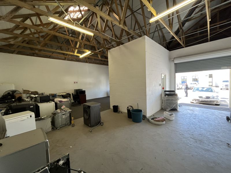 Spacious industrial utility area featuring exposed timber roof trusses, concrete flooring, and a large roller shutter door for easy access.