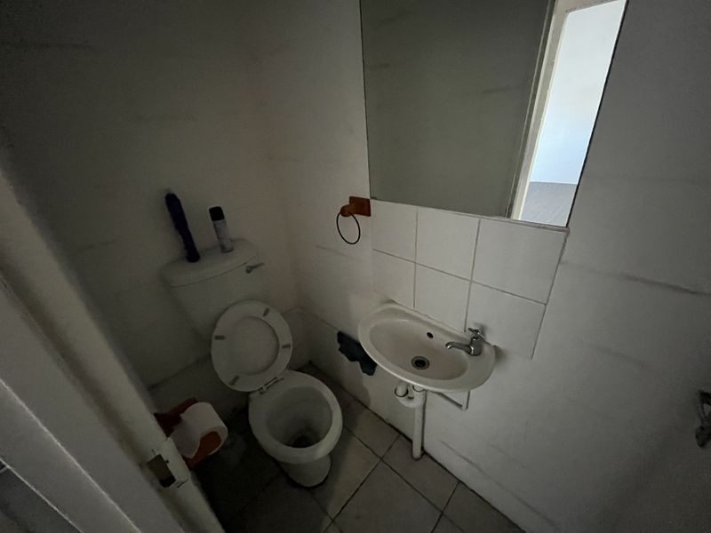 A compact industrial bathroom featuring a standard toilet, wall-mounted basin with tiled splashback, and a wall mirror.
