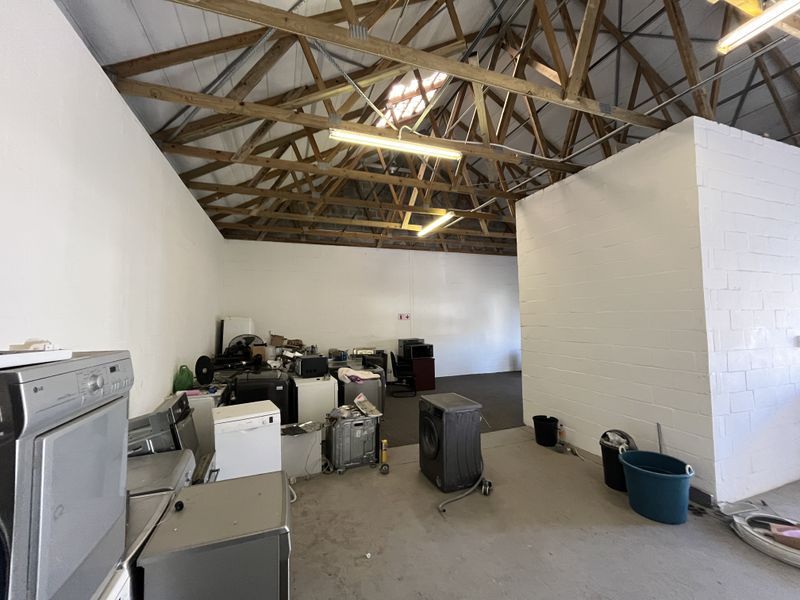 Spacious industrial utility area featuring exposed timber roof trusses, painted masonry walls, and durable concrete flooring, suitable for storage or workshop use.