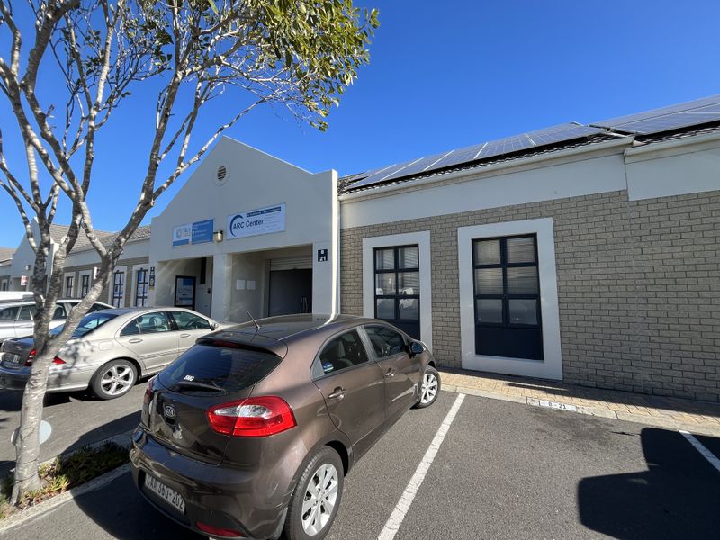Front elevation of an industrial unit featuring brick cladding, solar panels on the roof, and a dedicated parking bay.