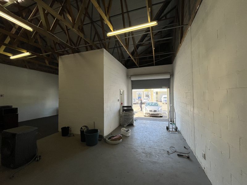 Spacious industrial utility area featuring exposed timber roof trusses, concrete flooring, and a large roller shutter door for easy access.