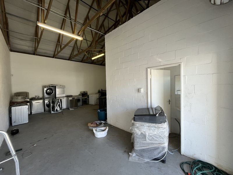 A spacious industrial utility area featuring exposed timber roof trusses, painted concrete block walls, and concrete flooring, suitable for storage or workshop use.
