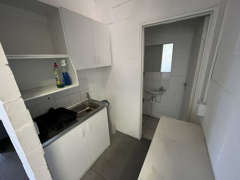 A functional scullery area featuring built-in cabinetry, a stainless steel sink, and an adjoining small washroom with a wall-mounted basin.