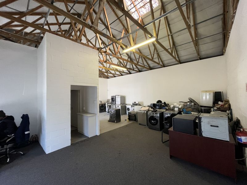 Spacious industrial utility area featuring exposed timber roof trusses, high ceilings with skylights, and functional open-plan layout suitable for storage or workshop use.