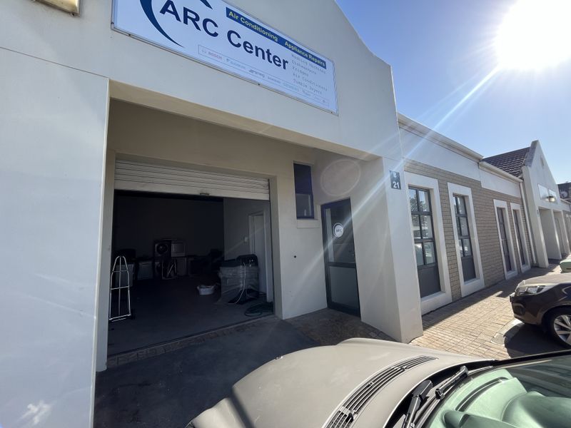 Front elevation of an industrial unit featuring a roller shutter door, signage, and paved access area.