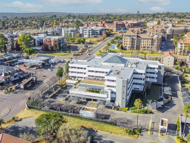 Aerial view of a commercial office building featuring extensive parking facilities, shade cloth carports, and secure perimeter access within a developed urban precinct.