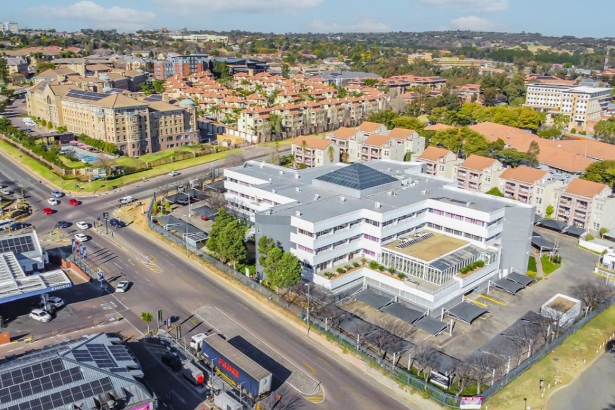 Aerial view of a multi-story commercial office building featuring a central skylight, extensive parking facilities, and secure perimeter fencing in a suburban setting.