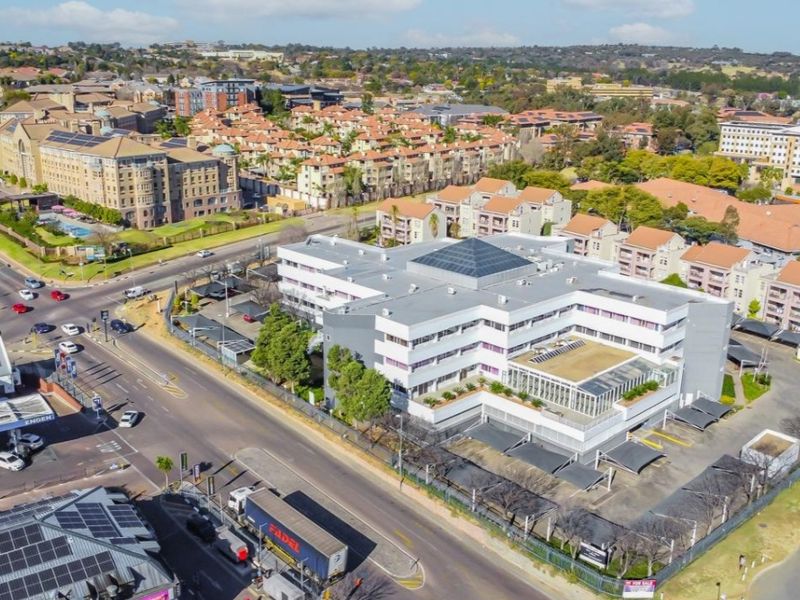 Aerial view of a multi-story commercial office building featuring a central skylight, extensive parking facilities, and secure perimeter fencing in a suburban setting.