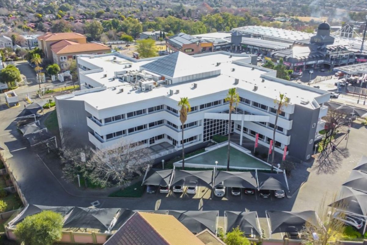 Aerial view of a multi-story commercial office building featuring a central skylight, extensive covered parking, and landscaped grounds in a suburban business district.
